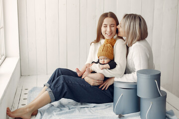 Family at home. Grandmother with daughter and grandson. Women in a white sweaters. Little kid in a cute yellow hat.