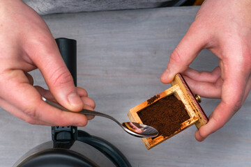 Fototapeta na wymiar a person makes coffee in a coffee machine picks up ground coffee with a spoon from a coffee grinder drawer