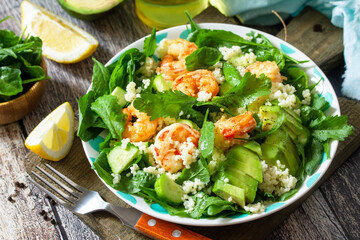 Food dieting concept. Couscous salad with arugula, avocado and grilled shrimps on rustic wooden table.