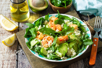 Food dieting concept. Couscous salad with arugula, avocado and grilled shrimps on rustic wooden table.