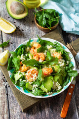 Food dieting concept. Couscous salad with arugula, avocado and grilled shrimps on rustic wooden table.