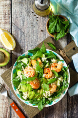 Food dieting concept. Couscous salad with arugula, avocado and grilled shrimps on rustic wooden table. Top view flat lay. Copy space.