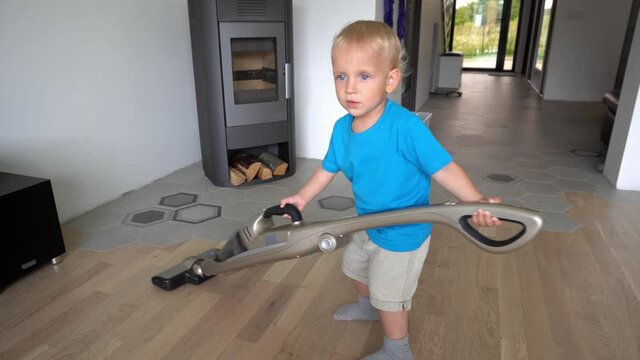 Baby boy with big vacuum cleaner on floor. Little mother helper son working