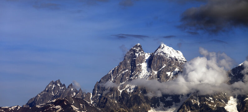Panoramic view on high rocky mountains with snow and glacier in clouds
