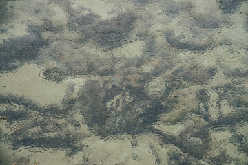 Atmospheric nature background with many black stones on sandy bottom in clear water of lake with rain circles. Transparent mountain lake. Minimal backdrop of clear water with rain circles and stones.