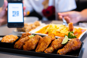 Selective focus to Fried chicken leg with blurry QR code tag on smartphone and customers is eating spaghetti.