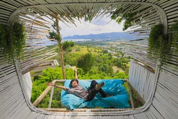 Asian man lying down on sofa bed  Asian tourist man is lying down on sofa bed near terrace in cafe outdoor with scenic view on mountains. Time to relax