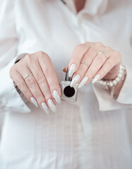 beautiful woman hands with long nails light white manicure and a bottle of nail polish