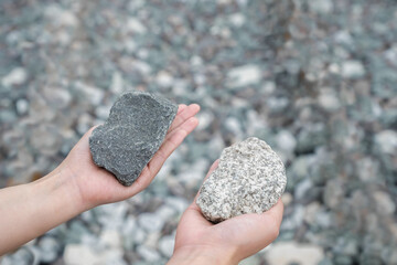 Hand hold rock and compare two choice between dark grey rock and white texture with blur ground....