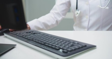 Close up of typing hands of beautiful Caucasian female doctor in white medical gown. Adult woman in glasses making reports and documentation on computer in hospital. Medicine, technology concept.