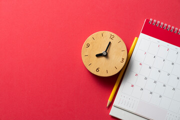 close up of calendar and alarm clock on the red table background, planning for business meeting or travel planning concept - obrazy, fototapety, plakaty