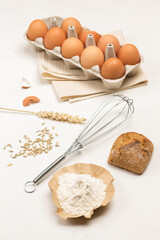 Flour on brown paper and bun. Tray with brown eggs. Metal whisk.