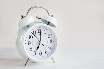 White clock alarm clock showing seven o'clock on a light background with copy space