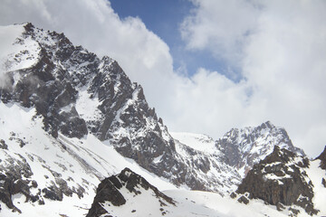 Fototapeta premium Alpine snow cliffs. Snowy cliffs high in the mountains, a clear winter sunny day, sharp peaks of the mountains in the snow against a blue sky with clouds, winter in the mountains