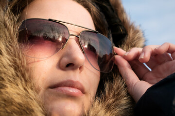 Girl in sun glasses and a fur hood against the blue sky