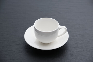 White textured coffee cup on a black textured stone slab, side view.