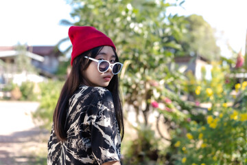 Beautiful happy teenage woman relaxing outdoors in park with a red hat and sunglasses, looking at camera on the green and yellow background poses to the camera in morning sunrise, lifestyle concept