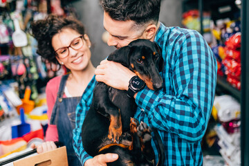 Happy couple buying toys and food for their Dachshund in pet shop.