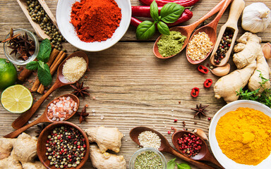 A selection of various colorful spices on a wooden table in bowls and spoons