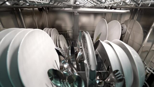 Forward dolly shot of dishwasher machine from inside, with dishes and silverware