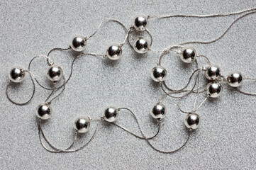 Women's jewelry in the form of silver beads on a silver thread with a clasp, photographed against a silver background.