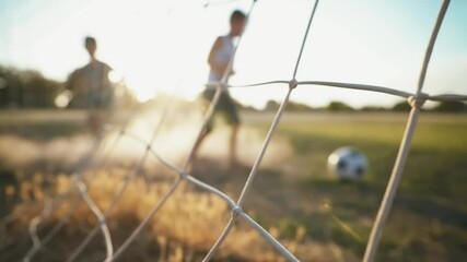 The brothers play football on the old field in the rays of the sunset. Local boys kick the ball. Football concept. Street sports in a poor area of a city or village. Training. Childhood memories.	 - Powered by Adobe