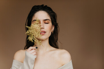Glad european lady with nude makeup posing with plant. Glamorous brunette female model chilling in...