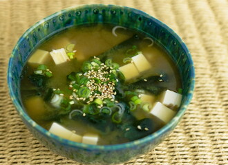 Miso soup with silken tofu, wakame seaweed, scallions and sesame in a green bowl.