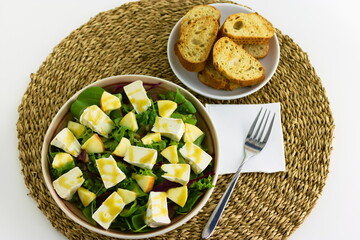 Mixed leaf salad with organic goat Camembert cheese and pears dressed with honey and mustard dressing on a plate. With toasted baguette slices on the side.