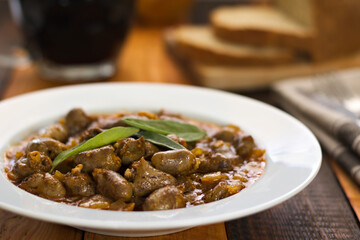 Stewed chicken hearts on a white plate garnished with sage.