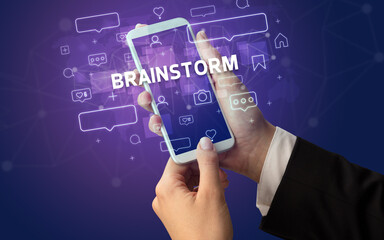 Female hand typing on smartphone with BRAINSTORM inscription, social media concept