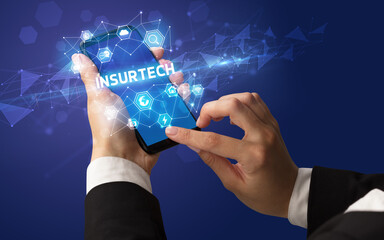 Female hand holding smartphone with INSURTECH inscription, modern technology concept