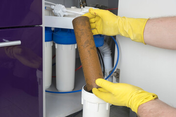 Plumber in yellow household gloves changes water filters. Repairman installing water filter...