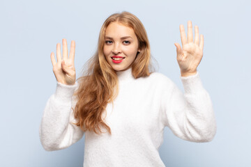 blonde woman smiling and looking friendly, showing number nine or ninth with hand forward, counting...