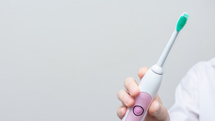 Woman's hand shows an electric toothbrush, white background, copy space, 16:9. Concept of caring for the oral cavity and healthy teeth with an smart toothbrush, cropped image