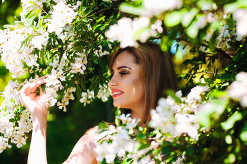 Fototapeta premium Outdoor portrait of young attractive woman in garden of blooming apple trees. Woman's Day. Female spring, summer fashion concept.