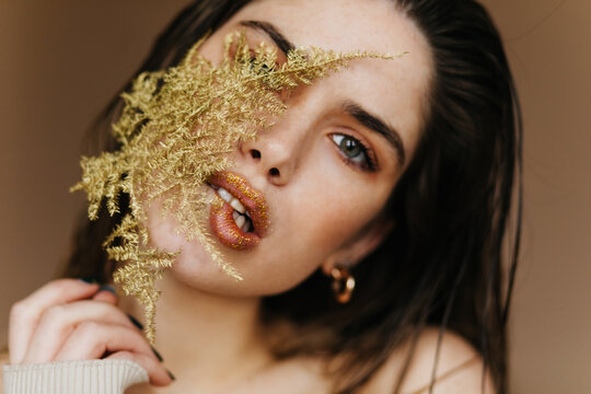 Charming Woman With Sparkle Makeup Holding Green Plant. Close-up Photo Of Cheerful Brunette Girl With Leaf.