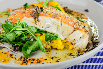A serving of grilled barramundi fish with paella risotto cake