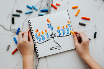 A girl drawing a celebration card with menorah (traditional candelabra) and candles for Happy Hanukkah jewish holiday. 