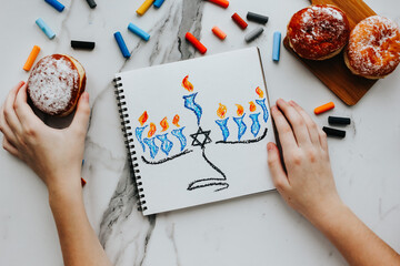 A girl drawing a celebration card with menorah (traditional candelabra) and candles for Happy Hanukkah jewish holiday. 