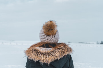 Rückansicht von junger Frau mit Wollmütze und Jacke im Schnee. Beobachten, Kälte, Winter.