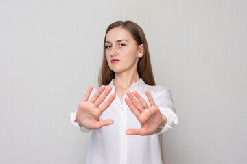 Young woman shows sign of stop. Girl in white shirt, portrait, white background, copy space