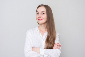 Young smiling girl with her arms crossed looks at the camera, white background