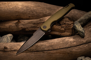 Knife with olive handle and black blade. Knife lying on wood.