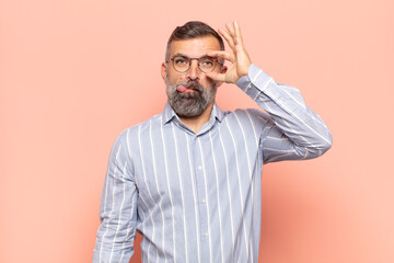 adult handsome man smiling happily with funny face, joking and looking through peephole, spying on...