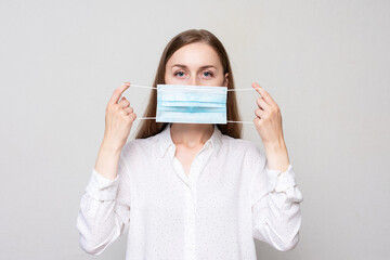 Young woman hides behind a medical mask, girl in white shirt, white background, copy space