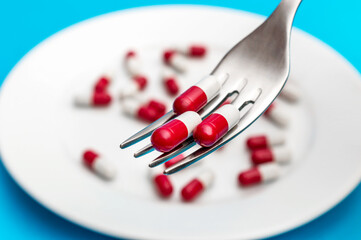 Medical capsules on the fork against plate with pills. Close up.