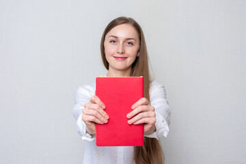 Beautiful young woman student shows red textbook, concept of education. Portrait, white background,...