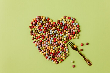 Not a perfect, partly eaten heart with fork made of colorful candies with lovely pastel green background. Minimal Valentine's day concept