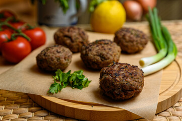 Homemade fried meatballs, served on wooden cutting board with tomatoes, onions and parsley